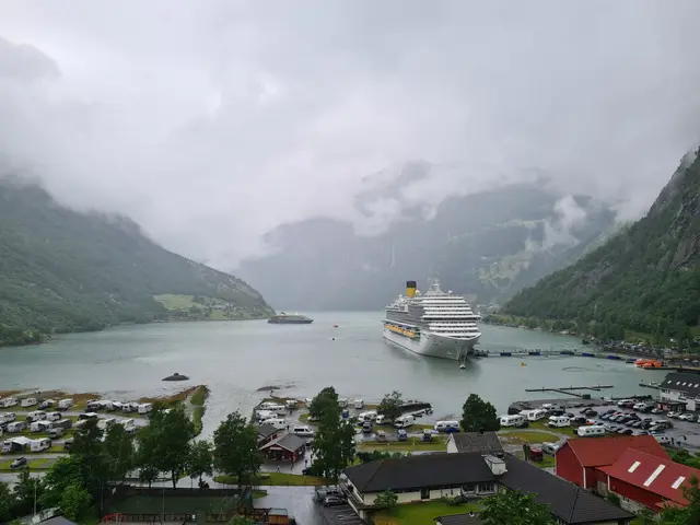 Zwei Kreuzfahrtschiffe liegen im wolkenverhangenen Geirangerfjord, davor Campingplatz und Dorf